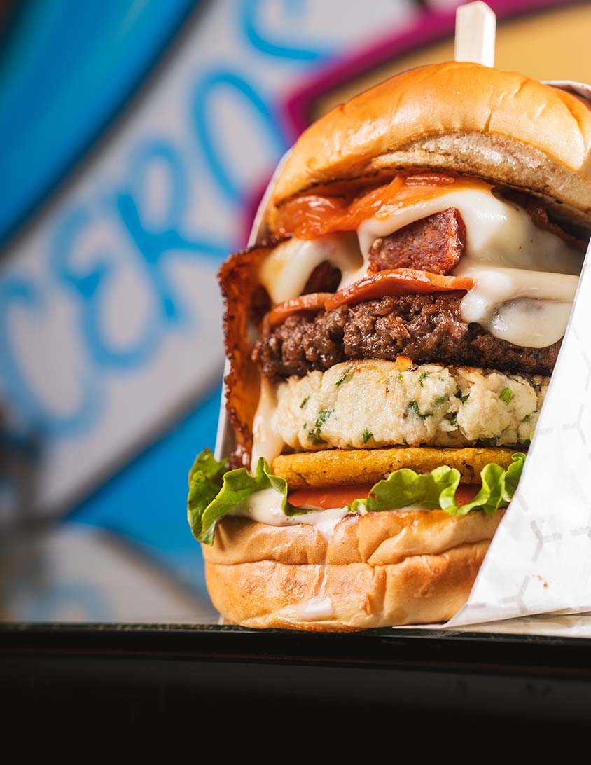 Towering specialty burger photographed against a colorful Miami restaurant mural.