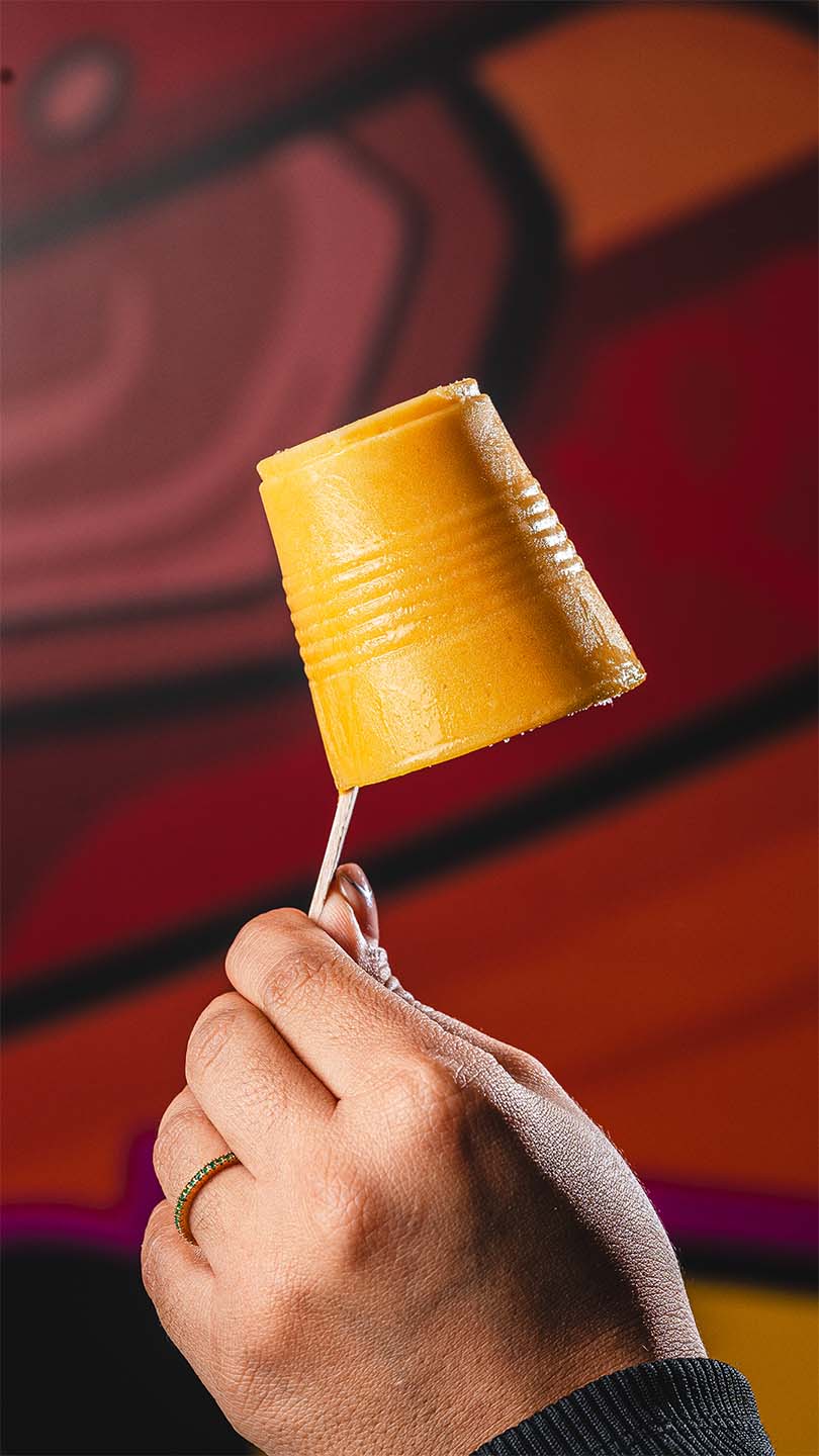 Golden tropical frozen dessert held against a warm graphic backdrop.