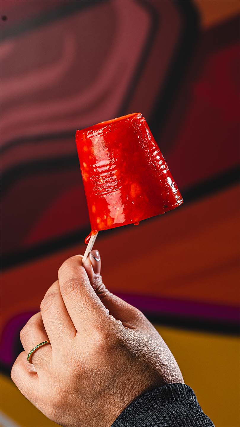 Glossy red frozen dessert held in a colorful restaurant setting.