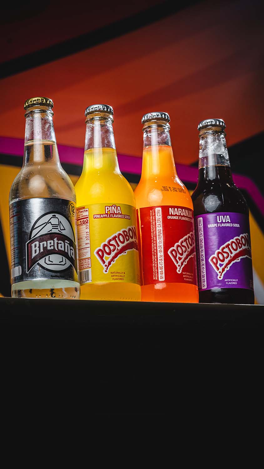 Lineup of Postobon and Bretaña bottled beverages in dramatic light.