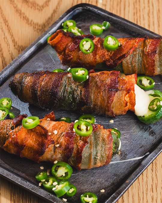 Bacon-wrapped peppers filled with cheese and finished with sliced jalapeño.