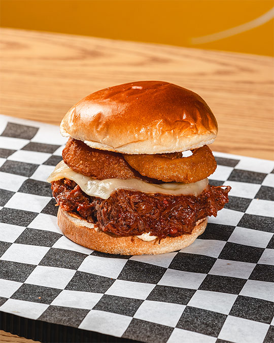 Pulled-meat sandwich with melted cheese and crispy onion rings.