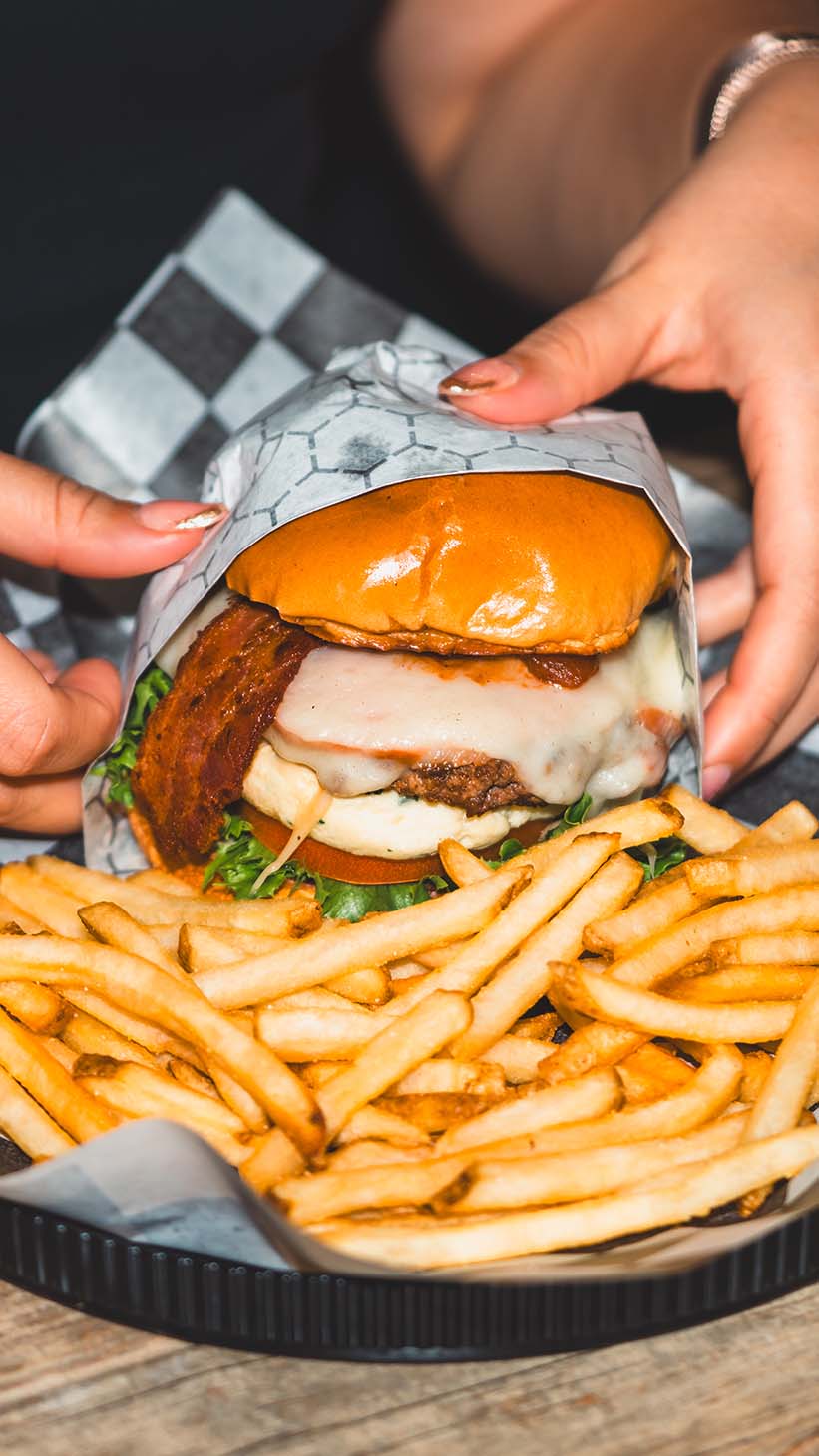 Burger and fries served as hands unwrap the sandwich for a lifestyle image.