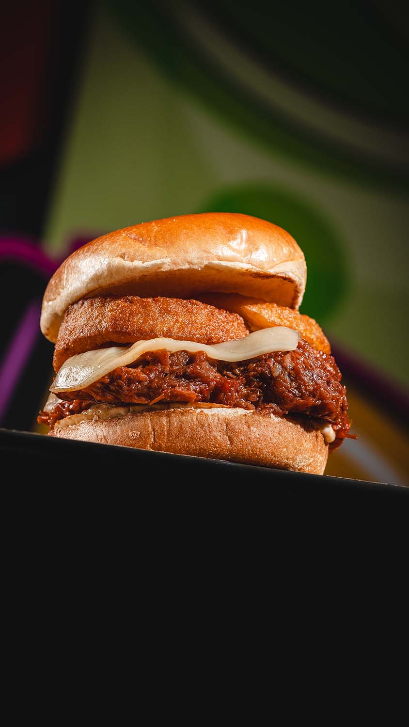 Pulled-meat sandwich with crispy onion rings photographed in moody light.