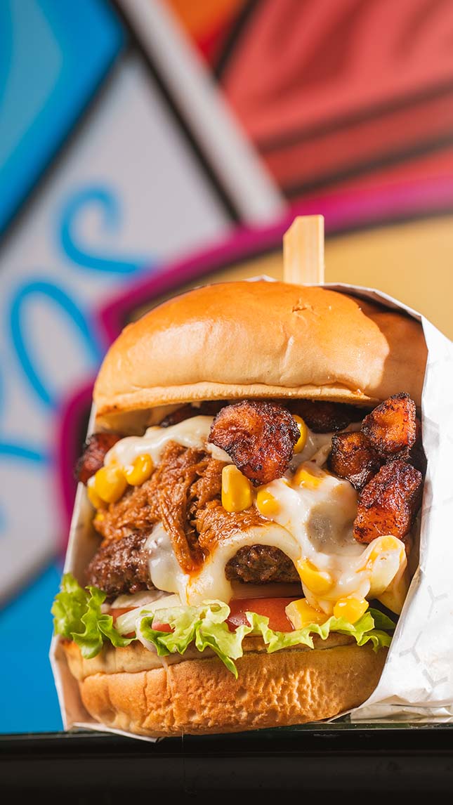 Loaded burger with pulled meat, melted cheese, corn, and caramelized plantain.