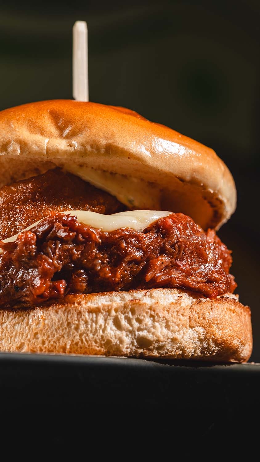 Extreme close-up of a saucy pulled-meat sandwich with melted cheese.
