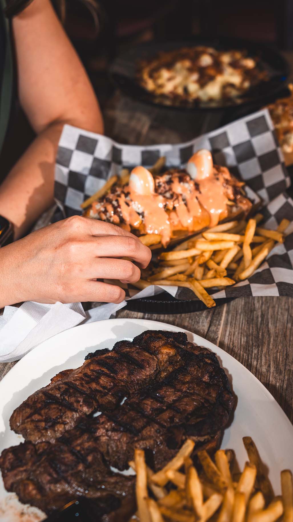 Candid restaurant table scene with loaded fries, steak, and shared plates.