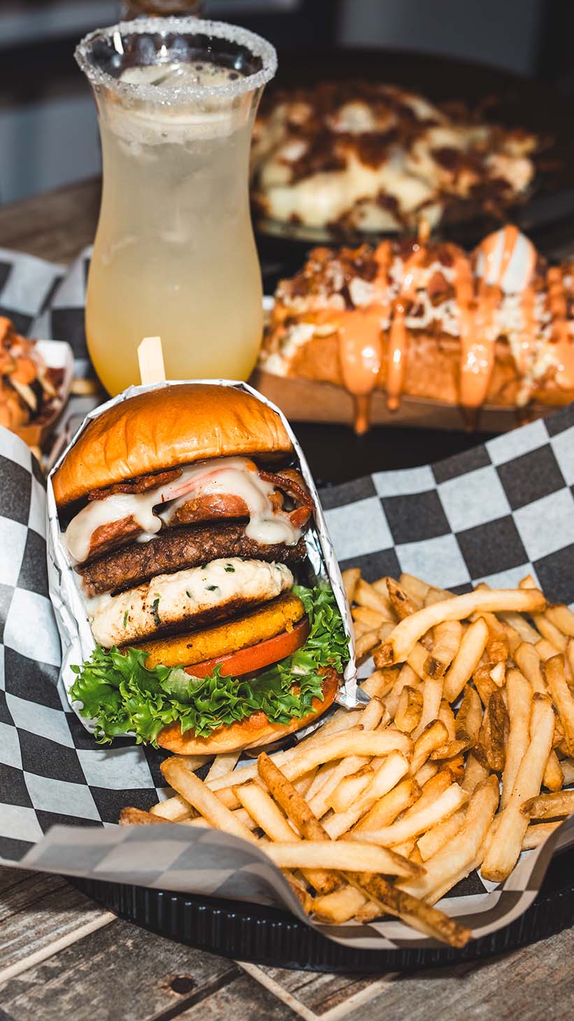 Signature burger, fries, loaded dishes, and a chilled drink presented together.