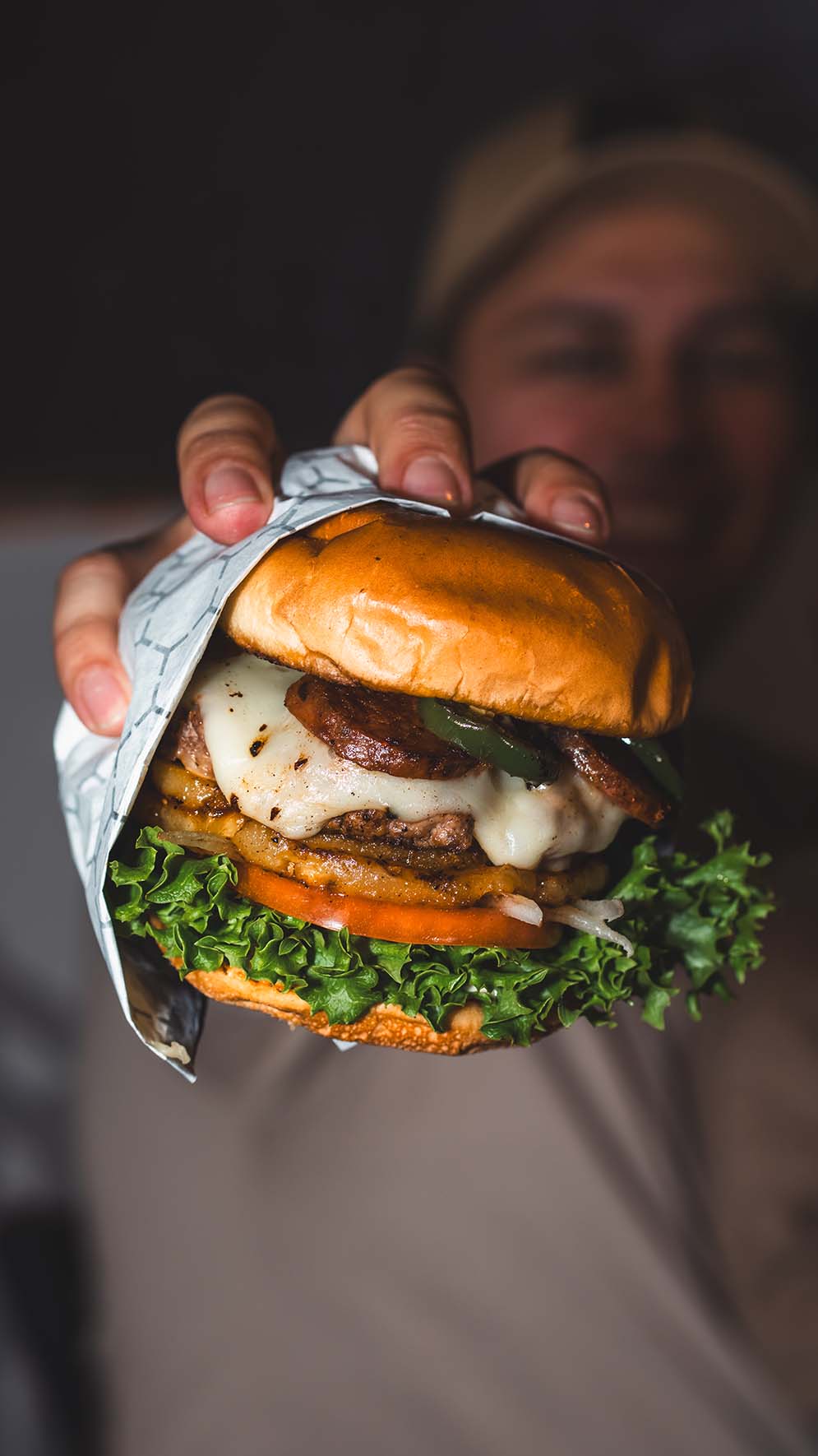 Guest presenting an oversized burger toward the camera in a dramatic portrait.