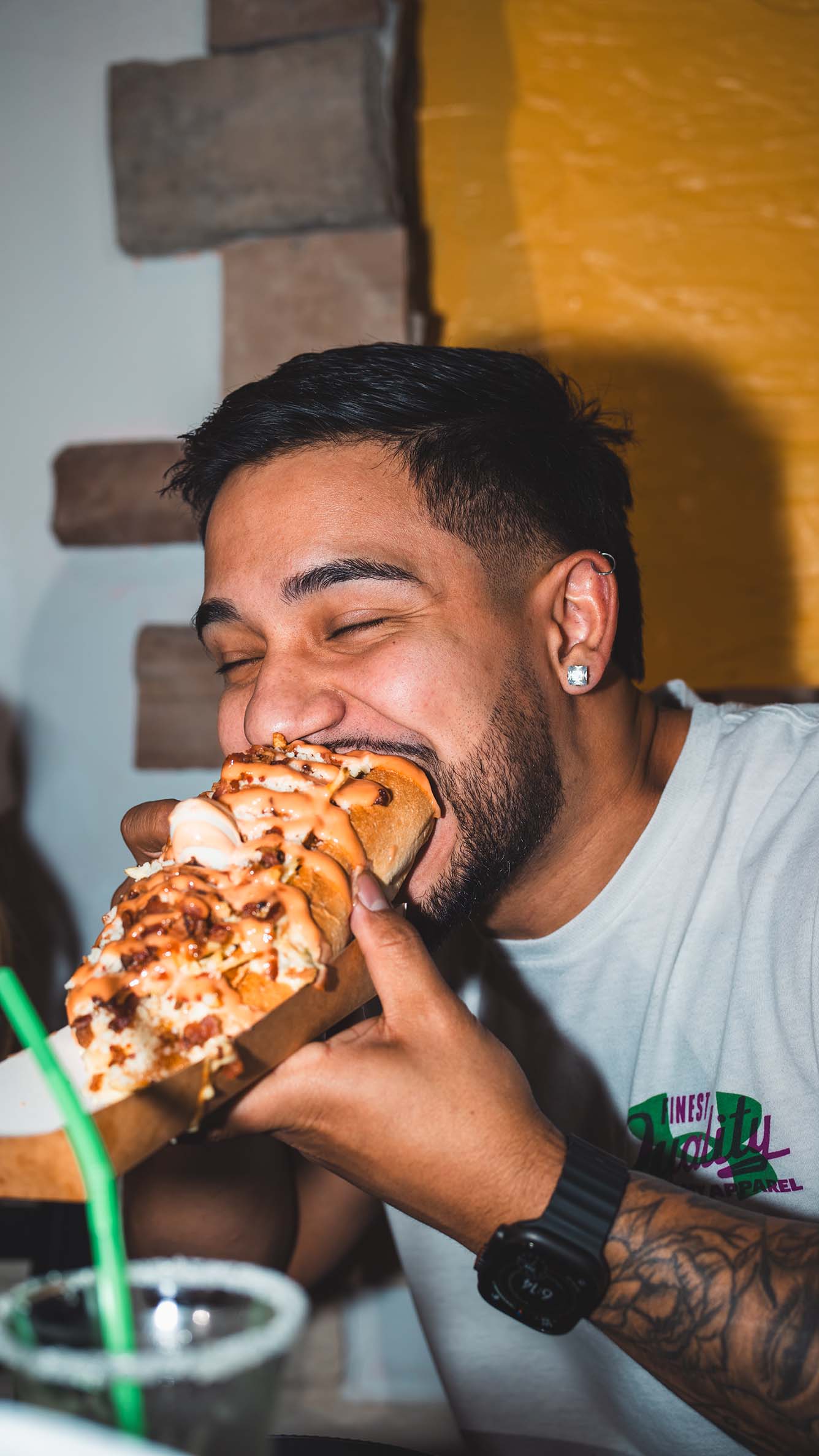 Restaurant guest taking a bite of a loaded hot dog.