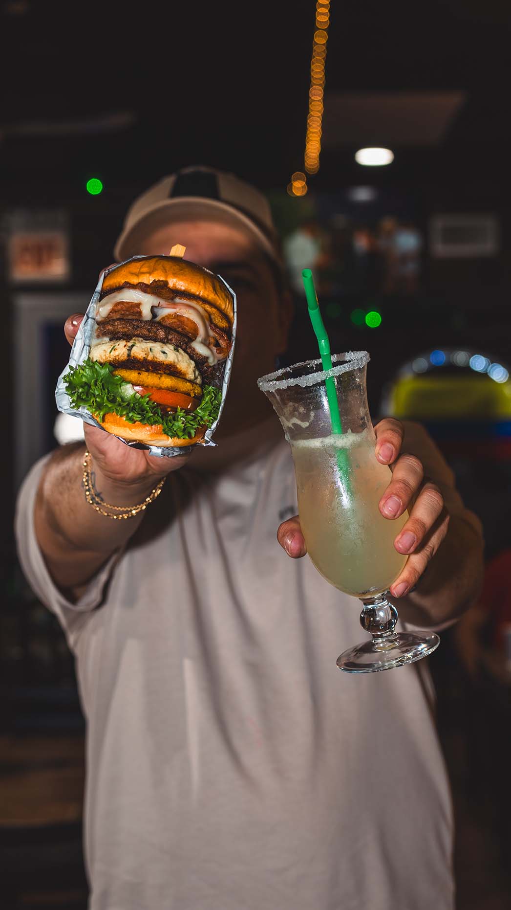 Guest holding a burger and a chilled cocktail inside the restaurant.