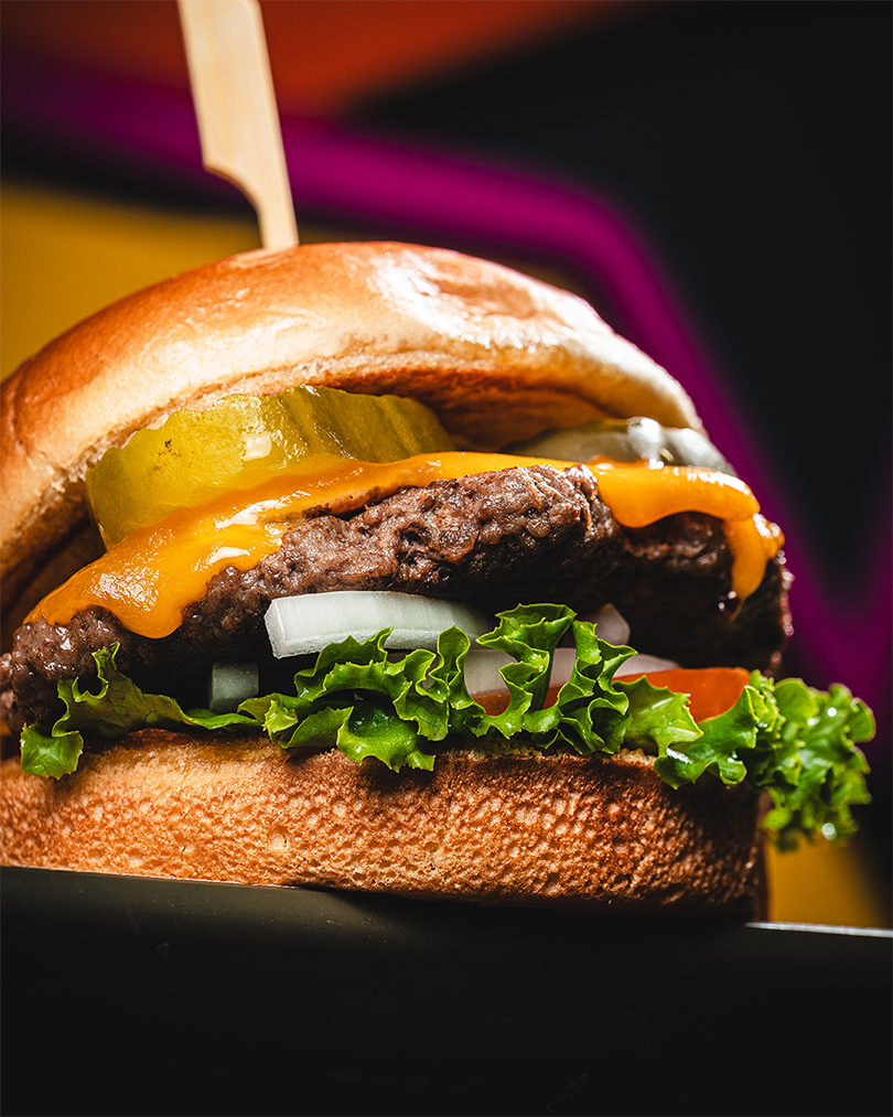 Classic cheeseburger with pickles, onion, lettuce, and tomato in dramatic light.