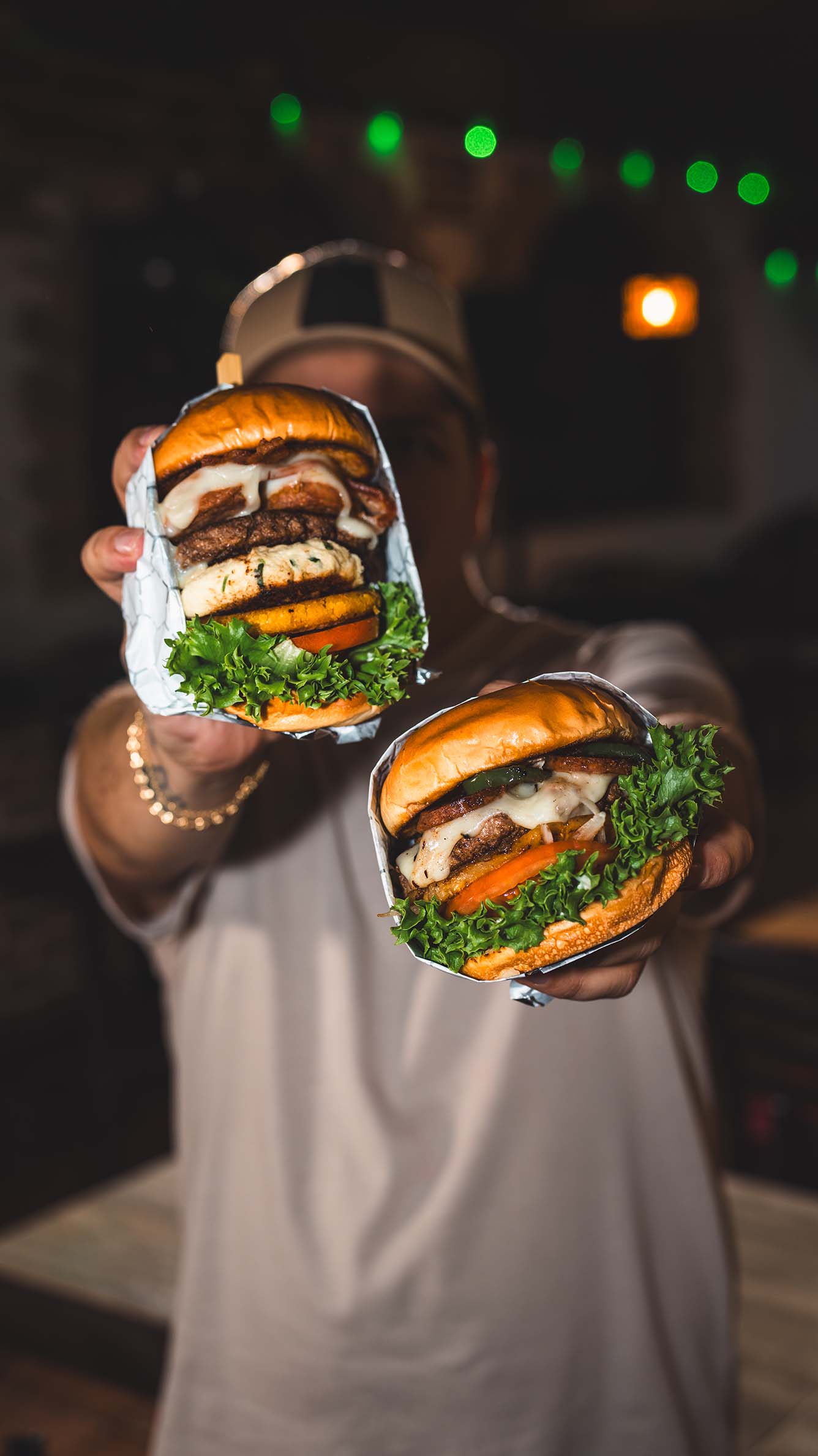 Guest presenting two signature burgers against colorful restaurant lights.