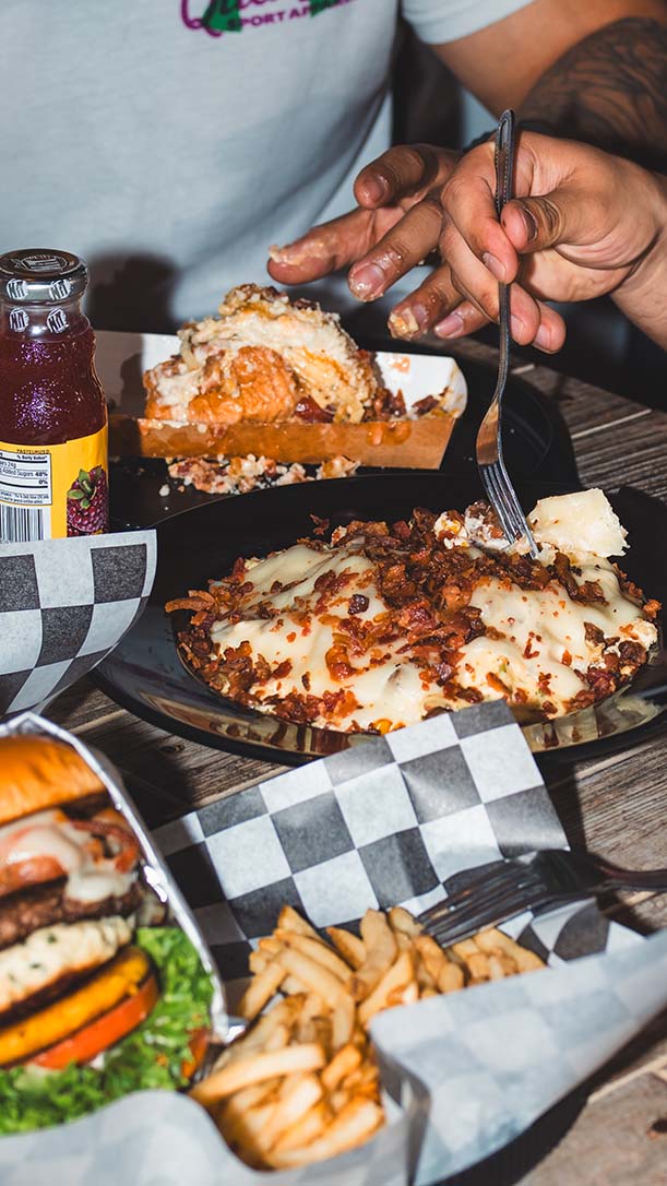 Shared dining table with burgers, fries, loaded dishes, and bottled soda.
