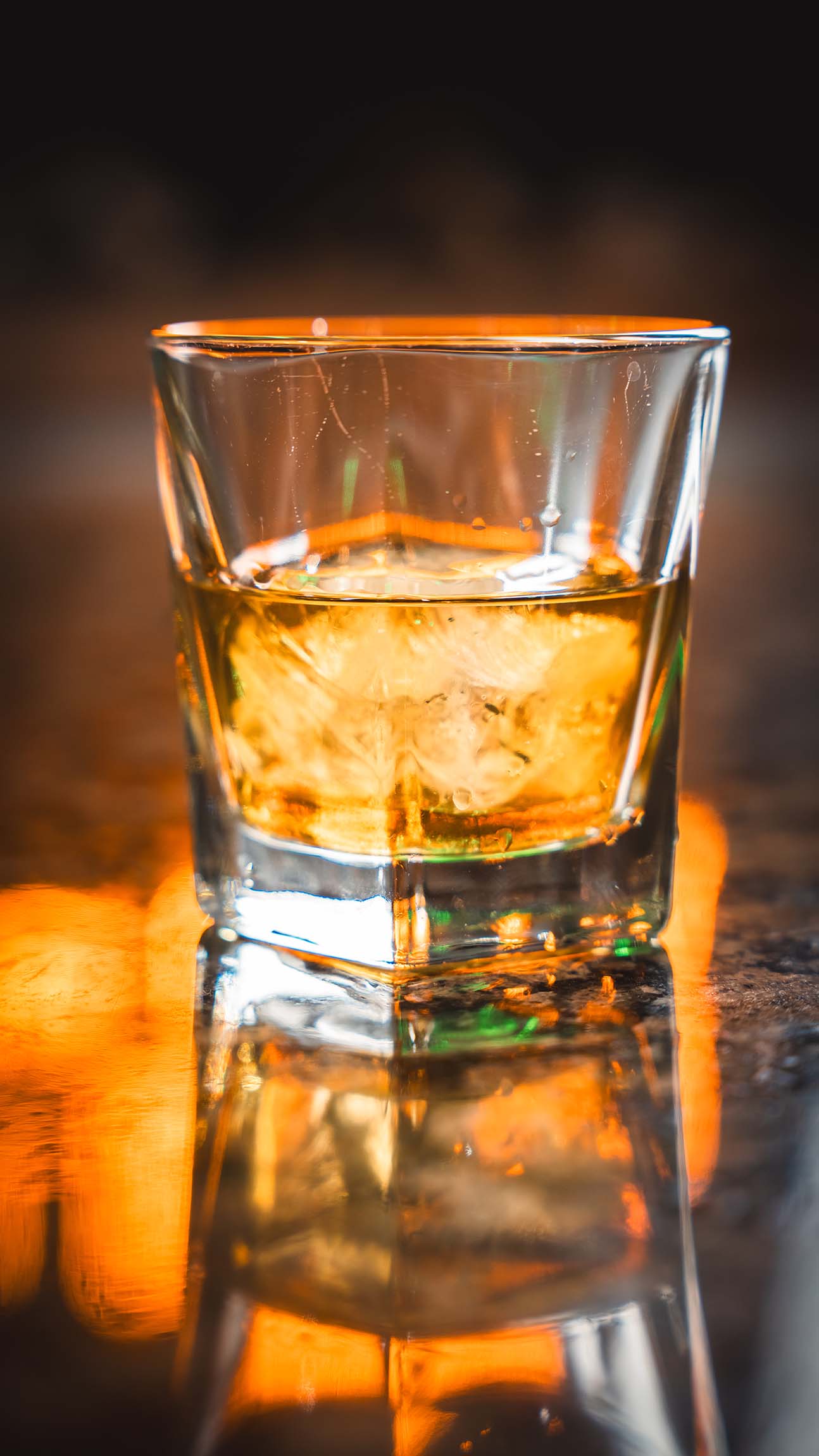 Amber spirit over ice photographed with warm reflected bar light.