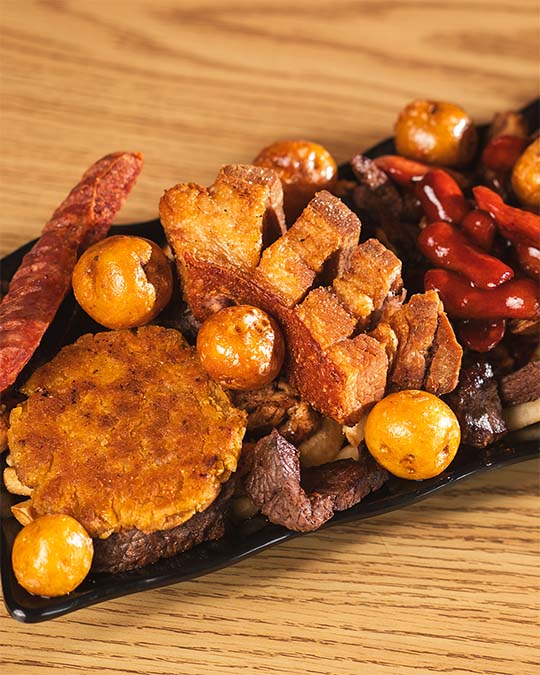 Mixed-grill plate with crispy pork, potatoes, sausage, and arepa.