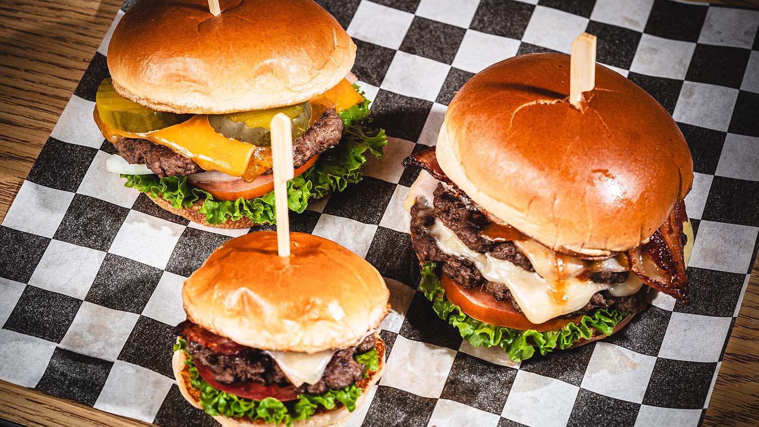 Three signature burgers presented together on black-and-white deli paper.