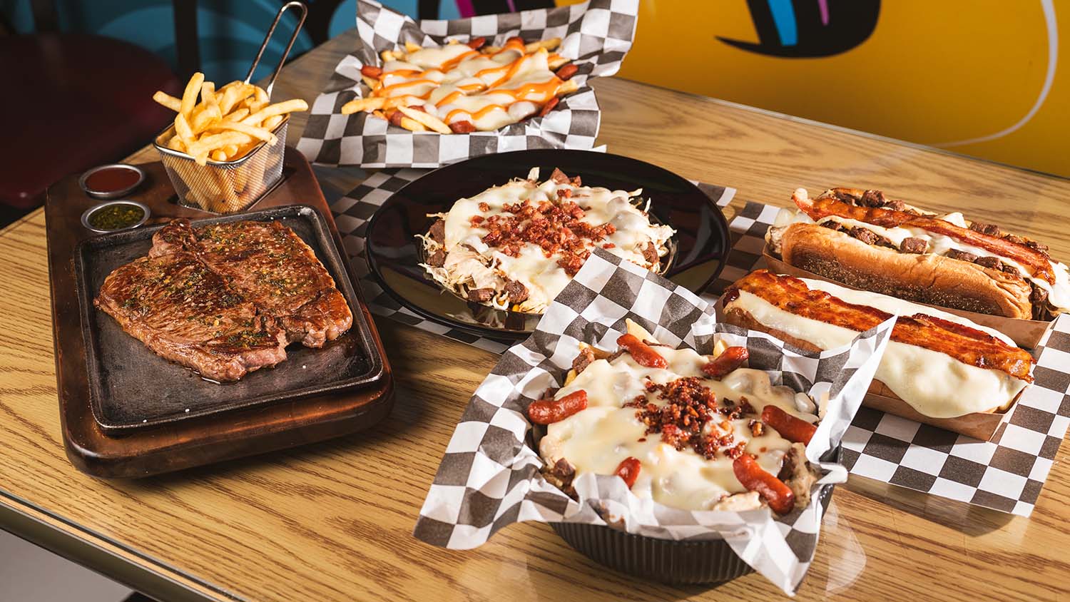 Restaurant table spread featuring steak, loaded fries, hot dogs, and sides.
