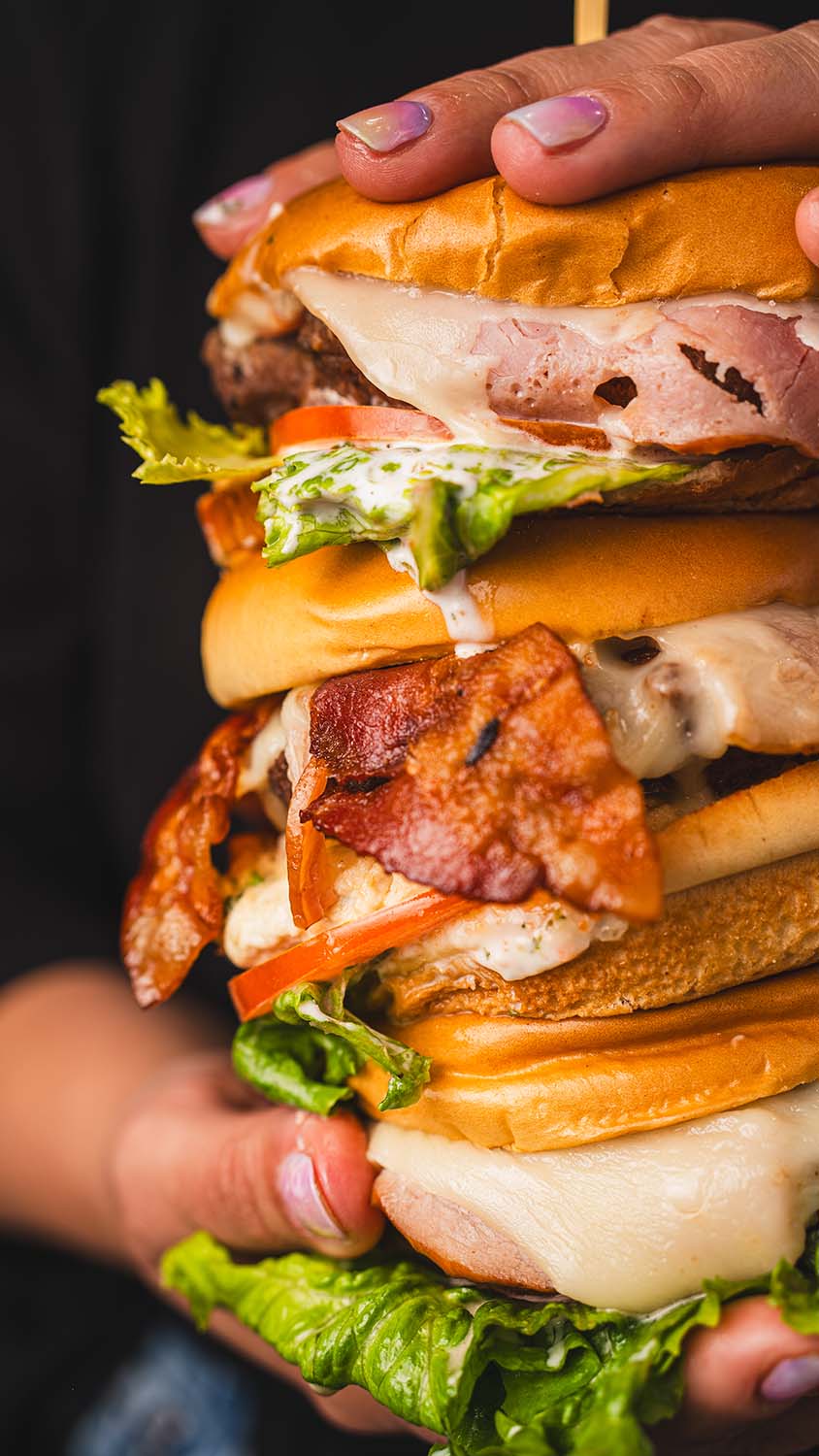 Stack of extravagant burgers with bacon, ham, cheese, and fresh vegetables.