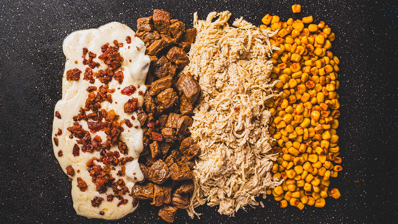 Overhead food composition with chicken, beef, corn, cheese, and bacon.