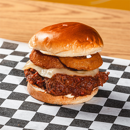 Pulled-meat sandwich with onion rings photographed for menu and delivery use.