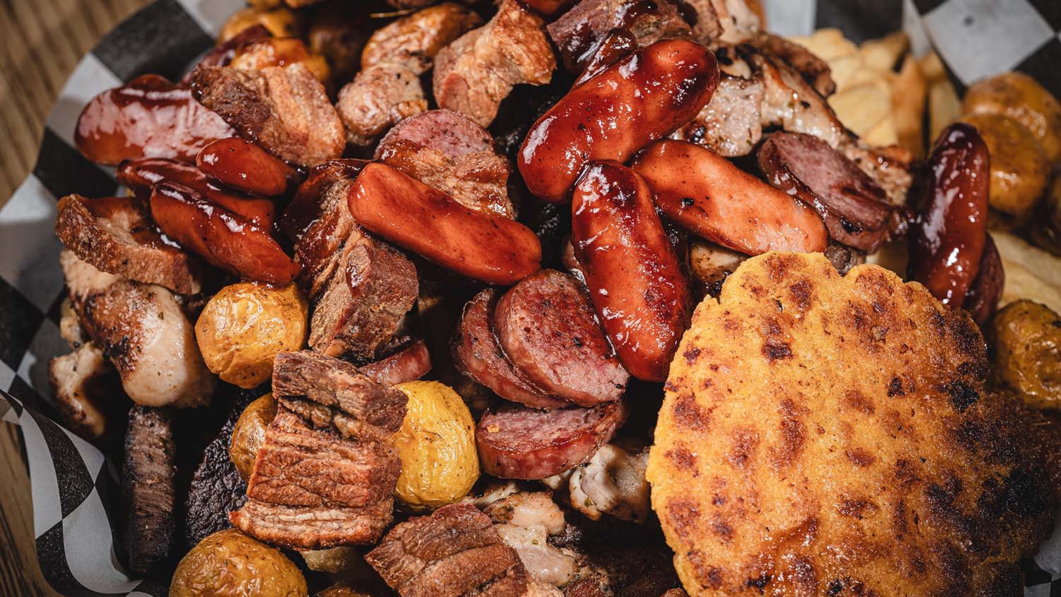 Overhead close-up of a mixed-grill platter with glazed meats and arepas.