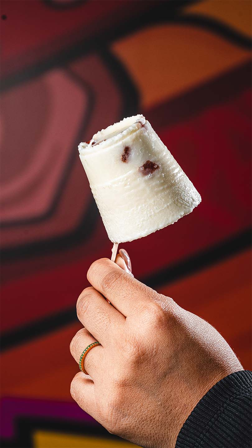Cream-colored frozen dessert held against a vibrant restaurant mural.